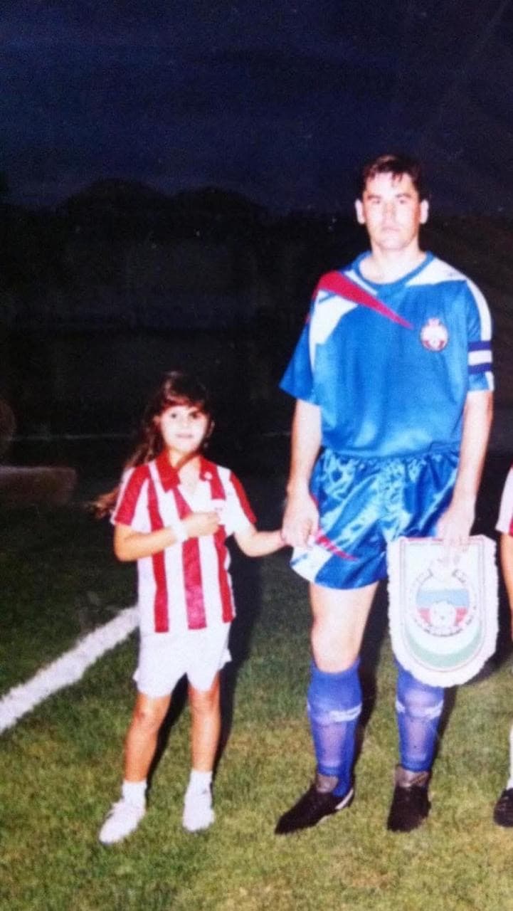 Carla Larini na infância ao lado do pai em um campo de futebol
